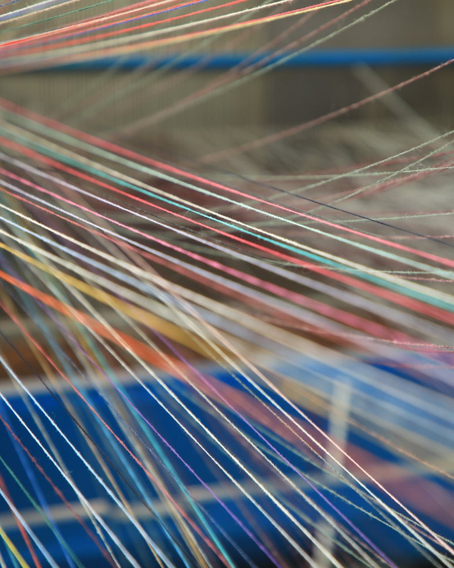 Multicoloured warp threads drawn across a knitting machine on our production floor